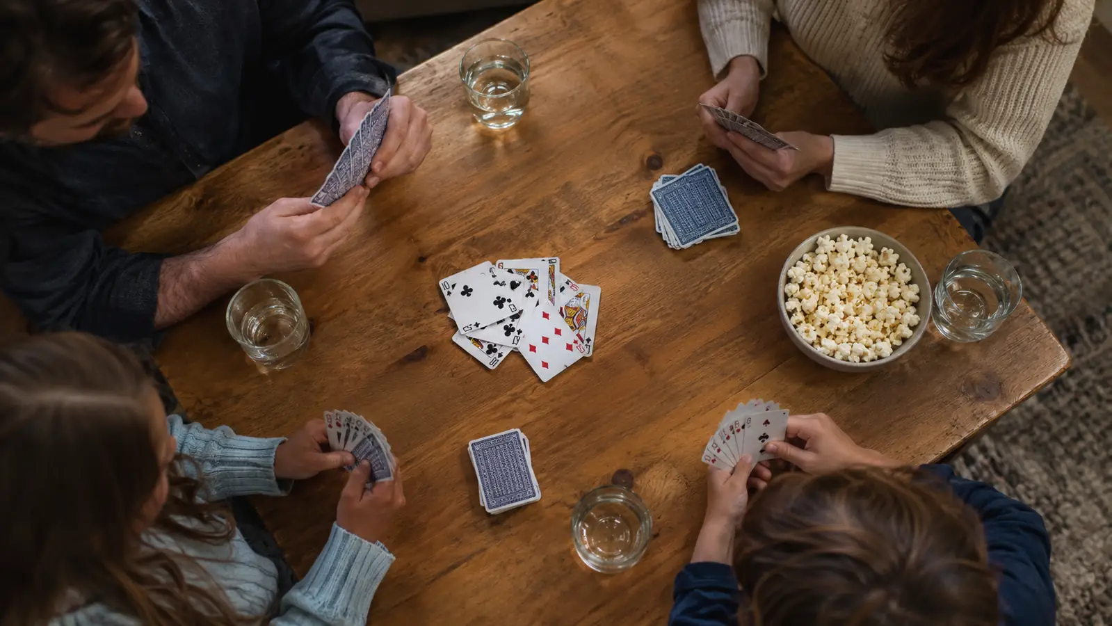 A top-down view of a card game spread out on a wooden table with a bowl of popcorn nearby